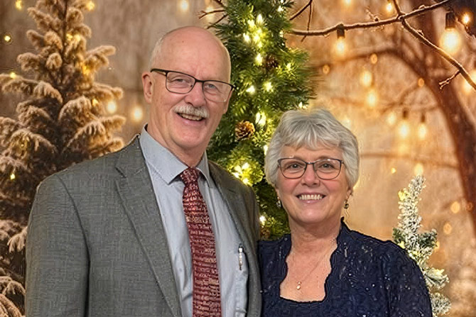 Man and woman in Sunday best posing in front of Christmas trees