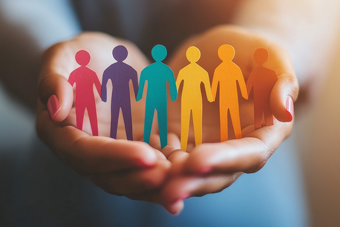 Hands holding paper cutouts of colorful people in a group