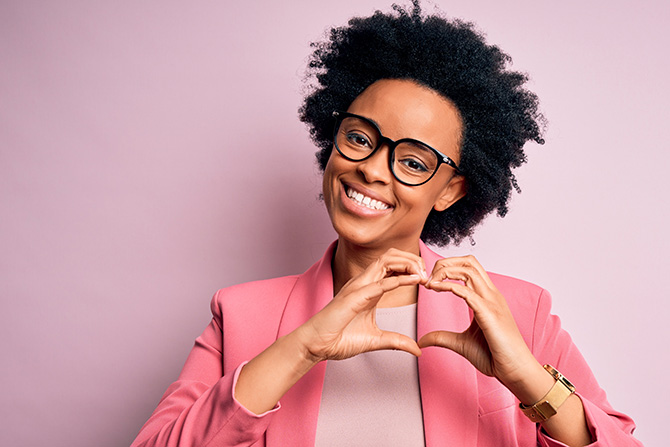 Smiling woman in pink jacket making heart shape with hands