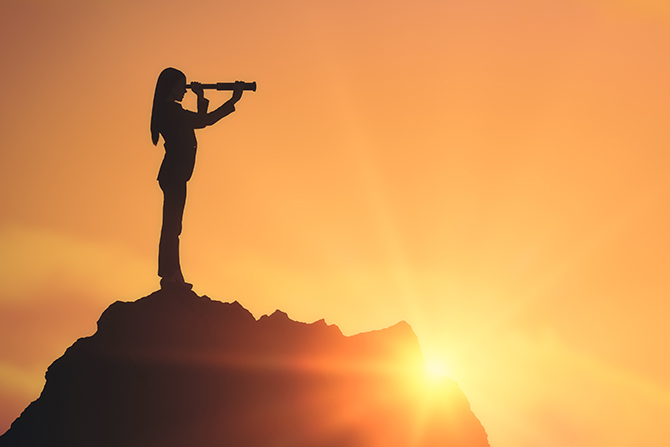 Silhouette of woman on mountain in front of sunset using telescope