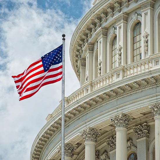 Close up of the US capital rotunda with a n American flag flying in front of it.
