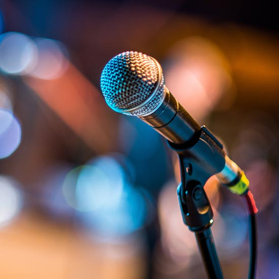 Convention-Speakers-FEATURE -- A corded microphone placed in a holder with a very blurred background.